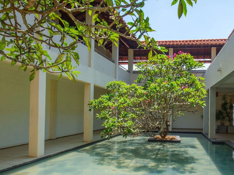 Dziedziniec z przezroczystym basenem i zielonym drzewem, otoczony białymi budynkami.