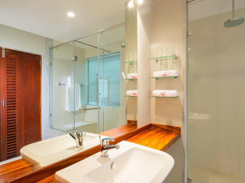 Nowoczesna łazienka z drewnianym blatem, umywalką, lustrem i szklaną ścianką prysznicową.