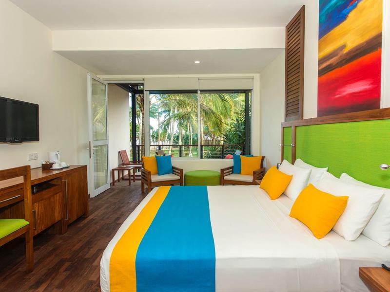 Nowoczesny pokój hotelowy z łóżkiem podwójnym, kolorowymi poduszkami i widokiem na palmy przez okna