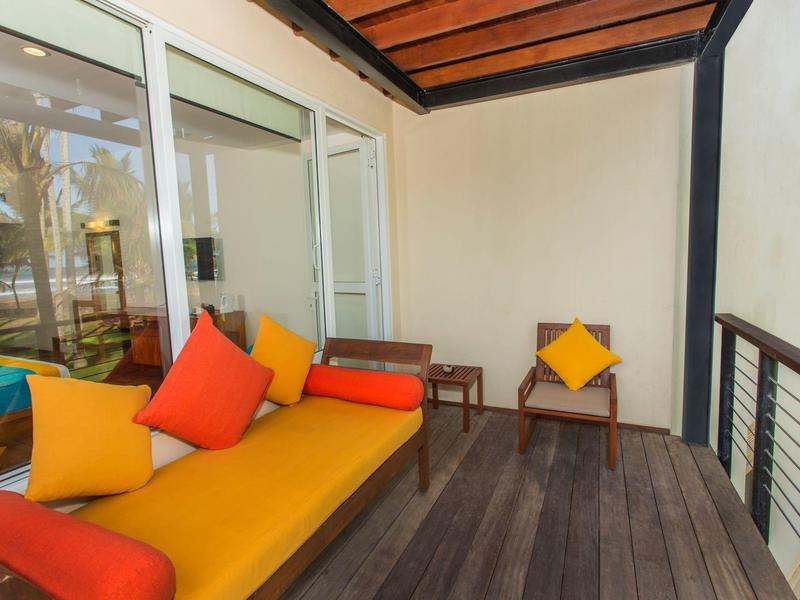 Balkon z żółtą sofą i kolorowymi poduszkami, drewniana podłoga i białe ściany.