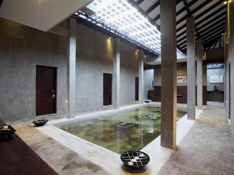 Espace intérieur avec une piscine rectangulaire entourée de murs et piliers en béton.