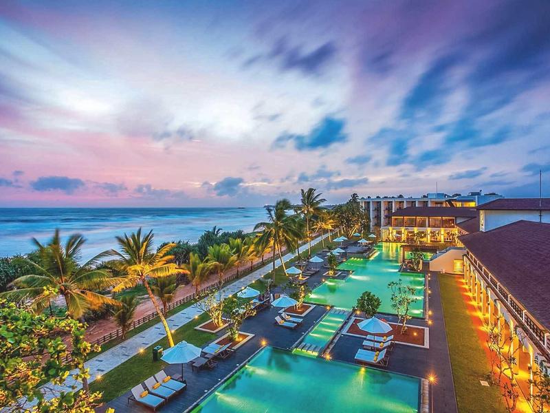 Espace piscine luxueux avec transats et vue sur la mer au coucher du soleil.