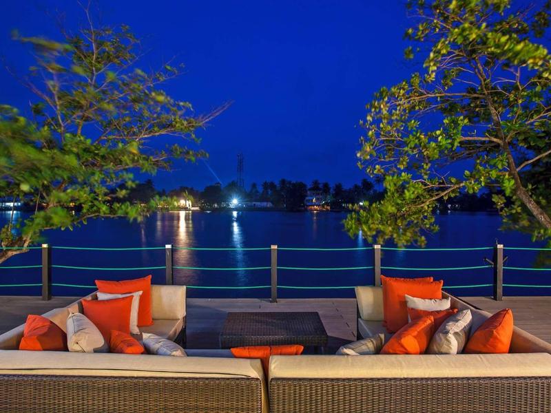 Coin salon confortable avec coussins au bord de l'eau la nuit avec arbres éclairés.