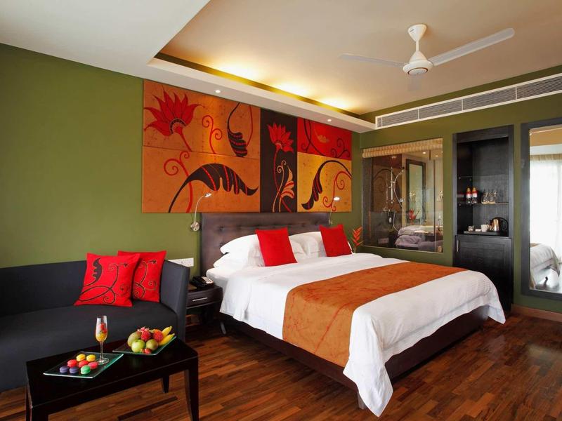 Chambre d'hôtel moderne avec lit double, canapé gris foncé, coussins colorés et œuvre murale.