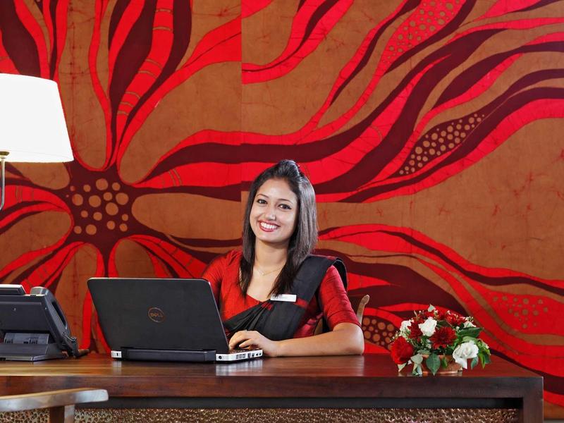 Réceptionniste assise à la réception avec un ordinateur portable devant un mur décoratif rouge.