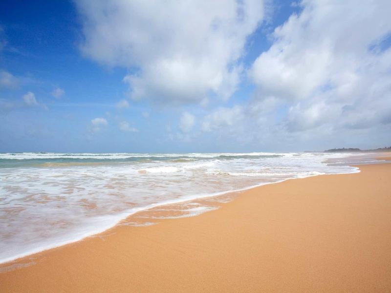 Plage de sable étendue avec des vagues douces sous un ciel bleu avec des nuages.