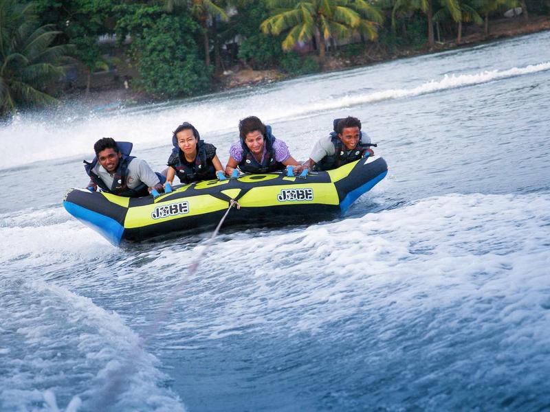 Trois personnes sont assises sur un bateau pneumatique jaune et bleu filant rapidement sur l'eau.