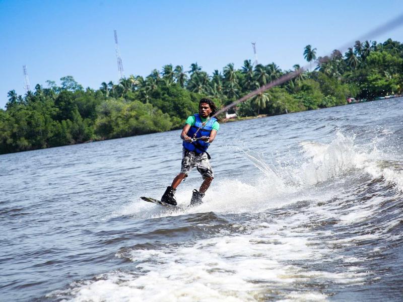 Personne faisant du ski nautique sur une rivière avec une rive boisée par temps clair.