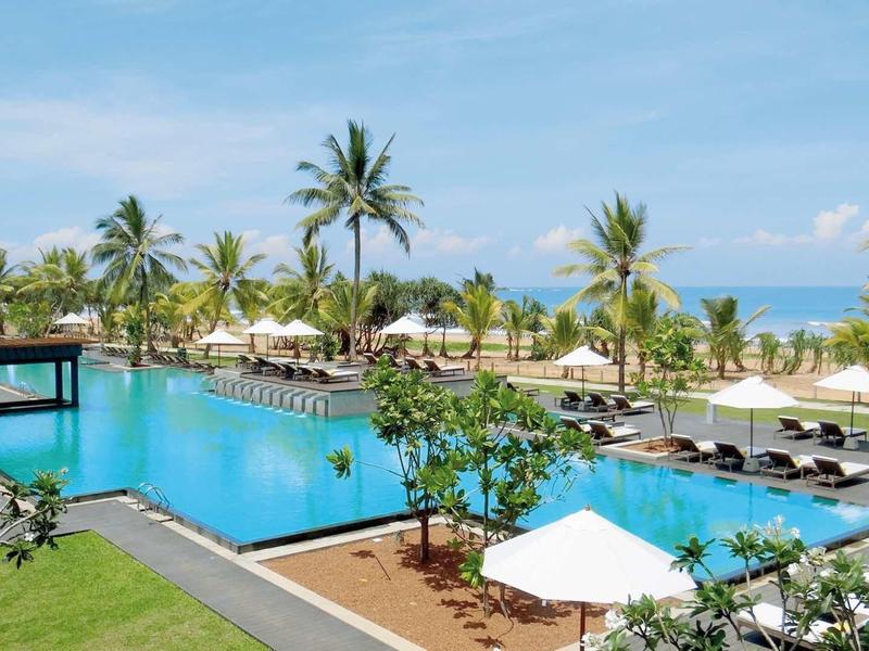 Grande piscine extérieure avec transats et palmiers sur la plage dans une station tropicale.