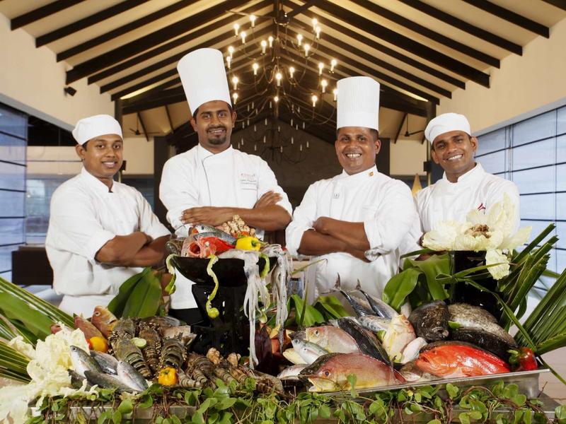 Quatre chefs en tenue blanche posent derrière une table garnie de poissons frais et d'herbes.