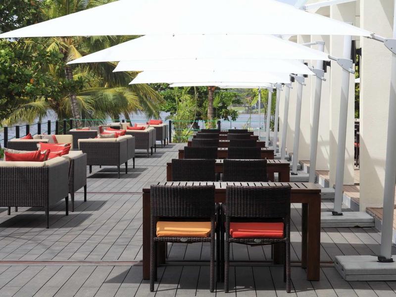 Espace extérieur moderne d'un hôtel avec des tables, des chaises et des voiles blanches.