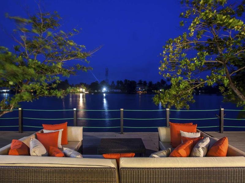 Coin salon confortable avec coussins sur terrasse face à un lac illuminé la nuit.