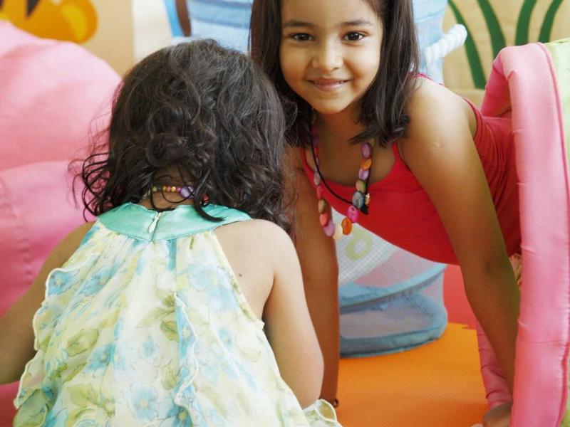 Deux filles jouent sur un sol en mousse colorée dans une aire intérieure ludique.