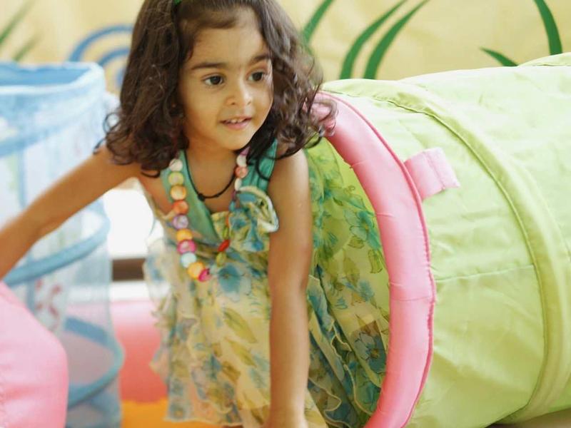 Enfant sortant d'un tunnel de jeu vert dans une salle de jeux colorée.