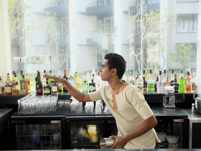 Homme derrière un bar d'hôtel attrapant une bouteille devant une étagère de spiritueux.