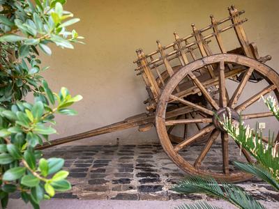 Alter hölzerner Wagen mit großen Speichenrädern steht auf gepflastertem Boden neben einer Wand.