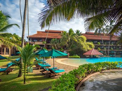 Hotelanlage mit Pool, Liegestühlen und Palmen unter blauem Himmel.