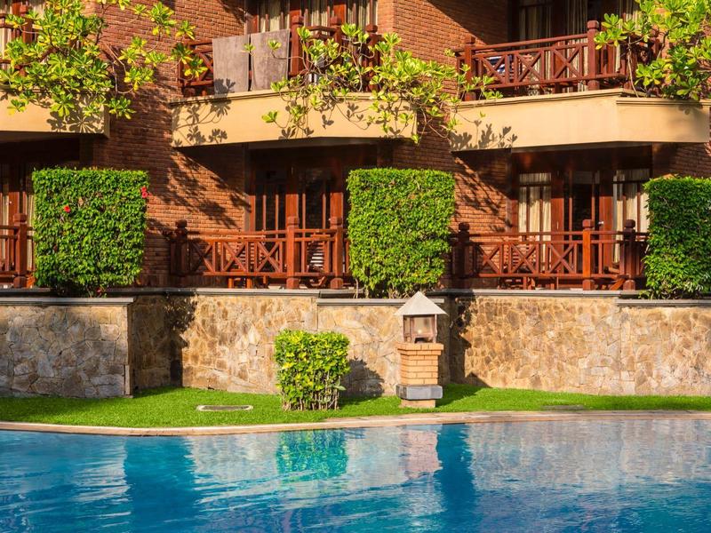 Uitzicht op een buitenruimte met zwembad, tuin en balkon voorzijde van een huis in zonlicht.