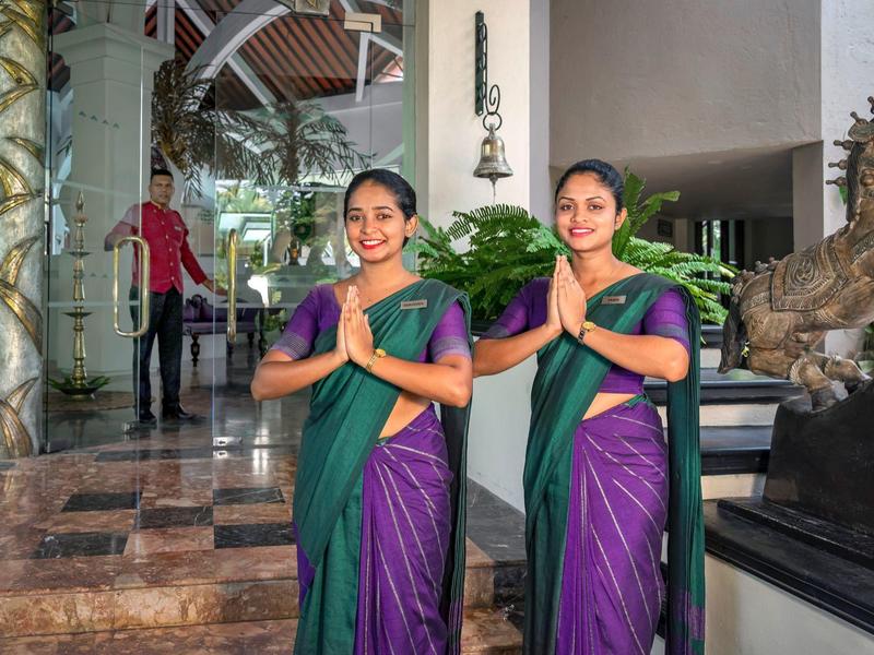 Twee vrouwen in traditionele sari's verwelkomen gasten bij een hotel lobby ingang.