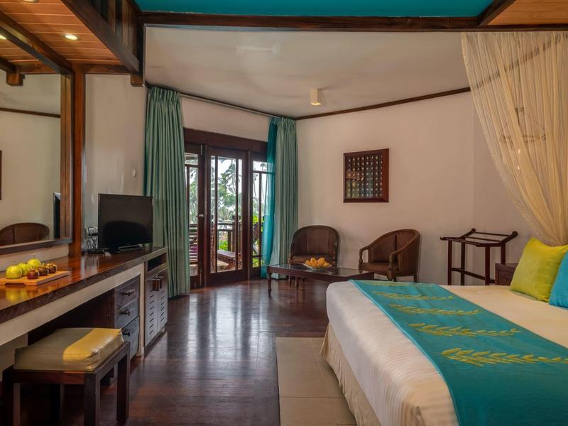 Gezellige hotelkamer met tweepersoonsbed, bureau, balkon en zithoek in warme tinten.