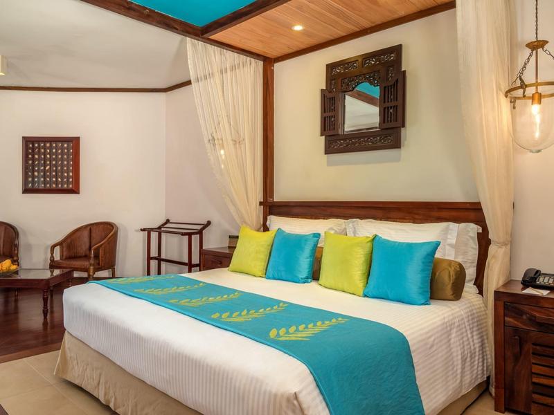 Gezellige hotelkamer met groot bed, kleurrijke kussens, houten meubels en wanddecoraties.