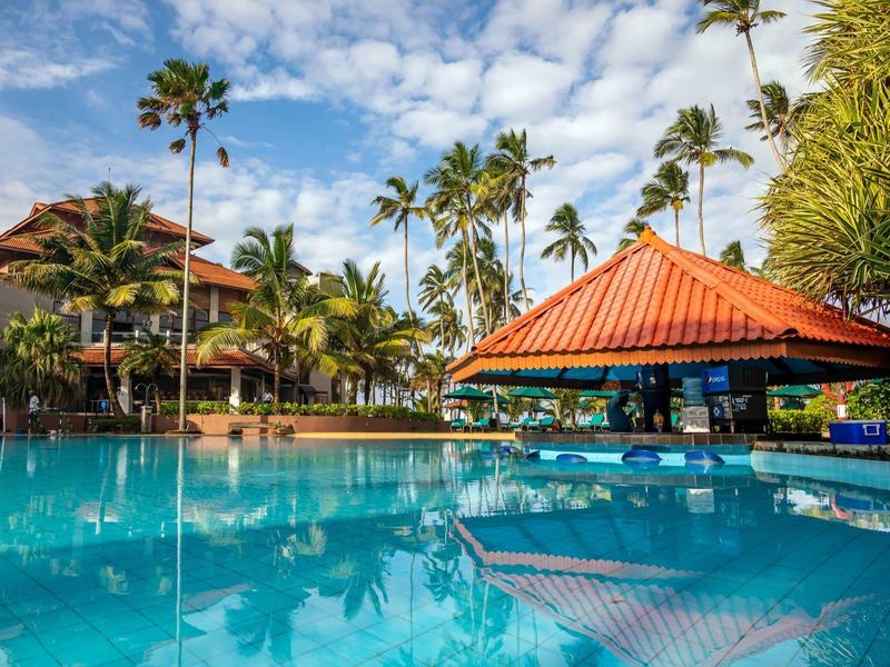 Hotelzwembad met een paviljoen en palmbomen onder een blauwe lucht.