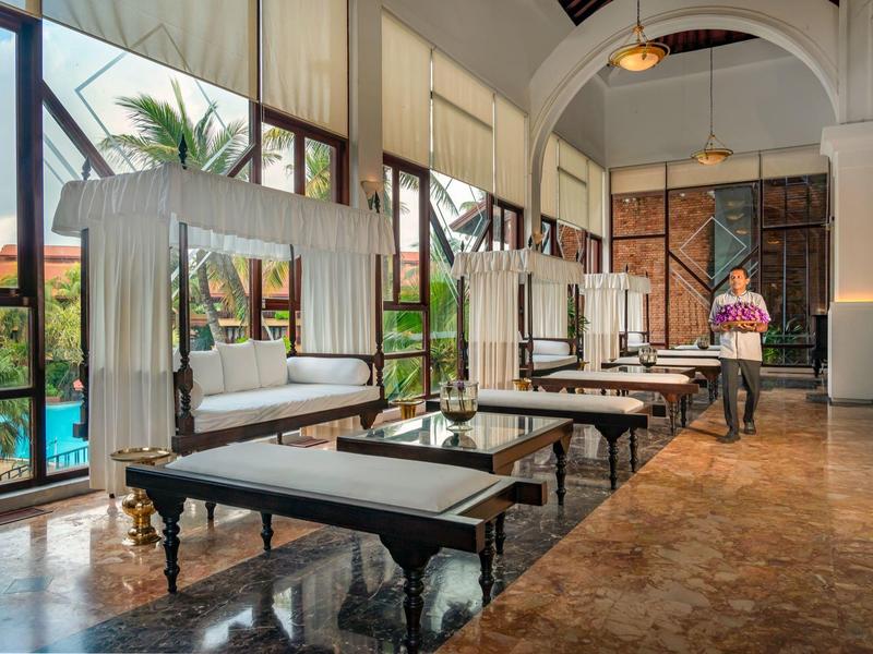 Elegante hotel-loungemeubels met dagbedden en kussens naast grote ramen en marmeren vloer.