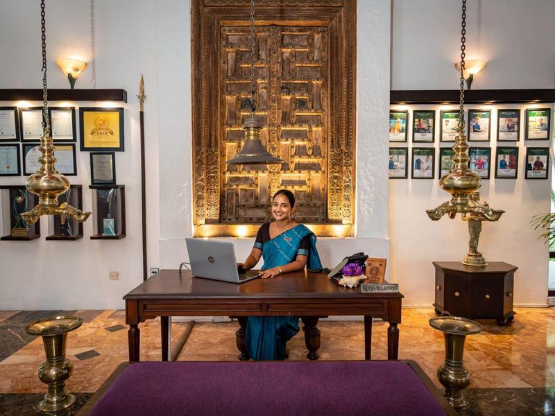 Vrouw in traditionele kleding zittend aan een houten tafel in een elegante, cultureel geïnspireerde kamer.