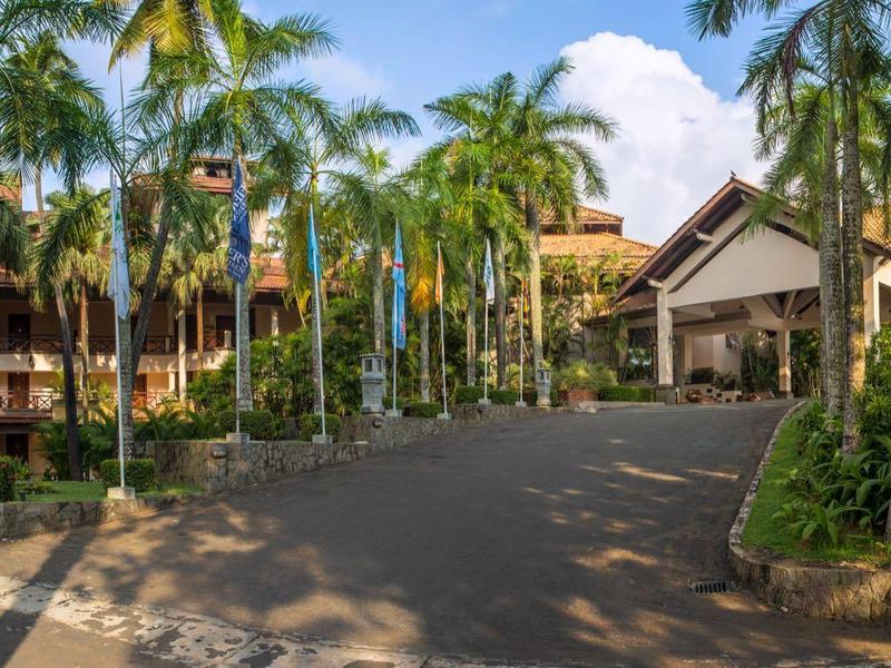 Entreegebied van een hotel met palmbomen en een grote boog bij een zonnige hemel.