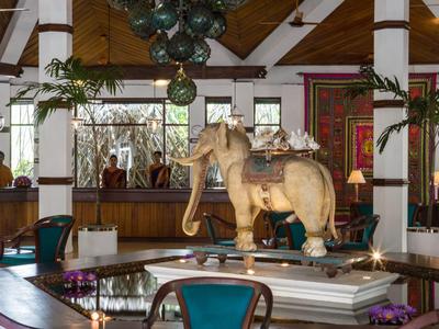 Interiér hotelu s dřevěným stropem, sochou slona a posezením s židlemi a stoly.