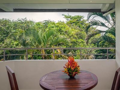 Balkon s malým dřevěným stolem, dvěma židlemi a květinovou dekorací na pozadí zelené džungle.