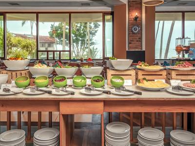 Bufet s čerstvým ovocem, dorty a talíři v světlé restauraci s výhledem do venkovní části.