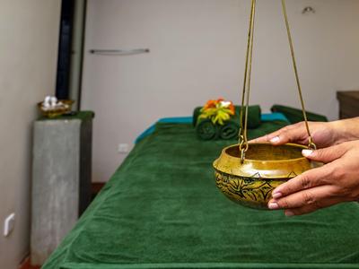 Behandlungsraum mit grünem Massagetisch und goldener Schale, in der Hände eine Blume halten.