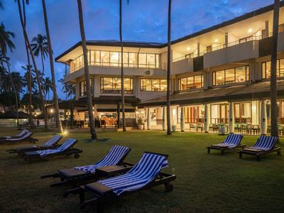 Osvětlená budova hotelu za soumraku s lehátky na trávníku.