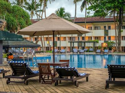 Lehátka a slunečníky u hotelového bazénu s palmami v pozadí.