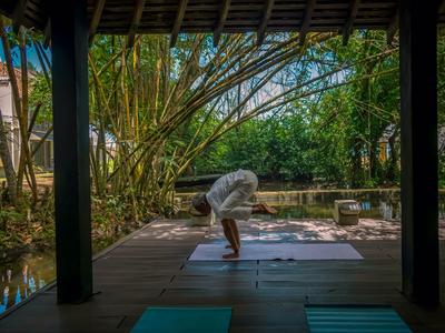 Person macht Yoga auf einer Terrasse mit Blick auf einen Teich und Bäume.