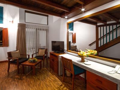 Příjemný hotelový pokoj s dřevěnou podlahou, posezením, velkým zrcadlem a dřevěným nábytkem.