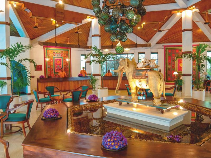 Světlá hotelová hala s dřevěným stropem, cihlovou zdí, útulnými posezeními a centrální fontánou.