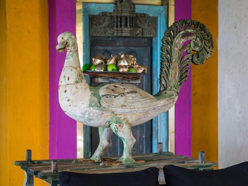 Velká kovová socha pávu před oranžovou a fialovou zdí uvnitř