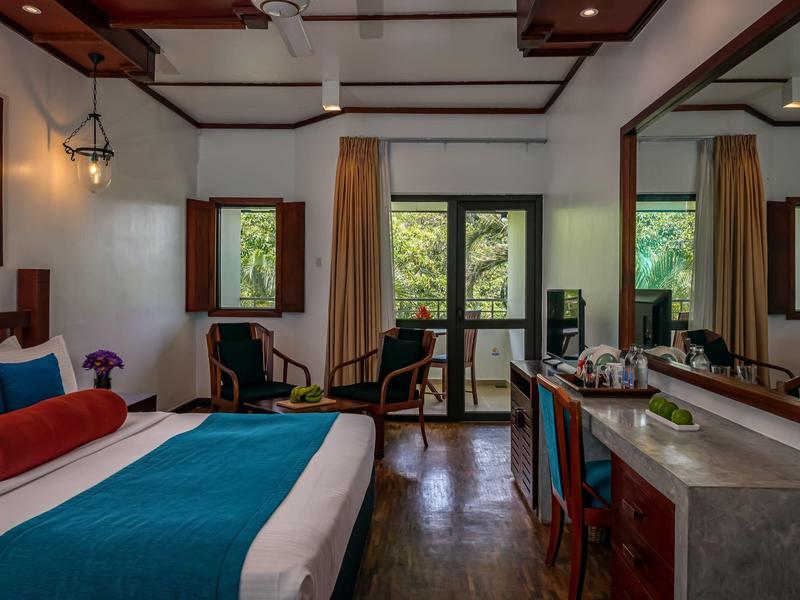 Světý hotelový pokoj s velkou postelí, posezením a okny s výhledem na stromy.