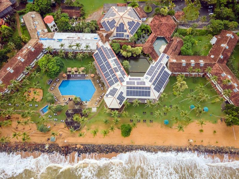 Letecký pohled na hotel s bazénem, zahradou a přístupem na pláž s vlnami.