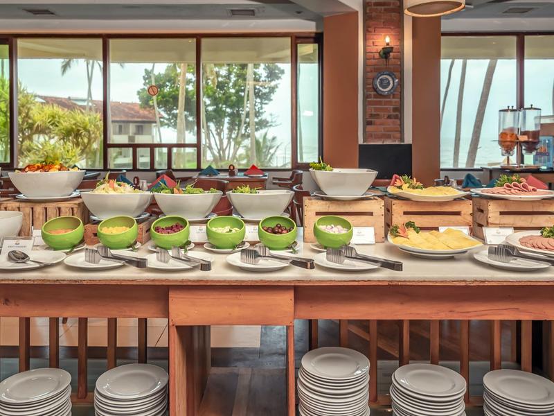 Bufet s čerstvým ovocem, dorty a talíři v světlé restauraci s výhledem do venkovní části.