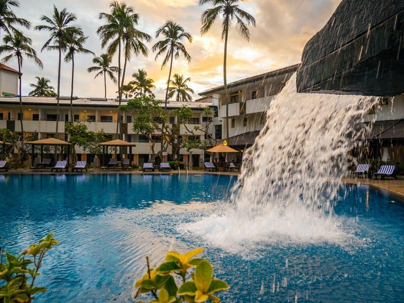 Hotelový bazén s vodopádem a palmami při západu slunce