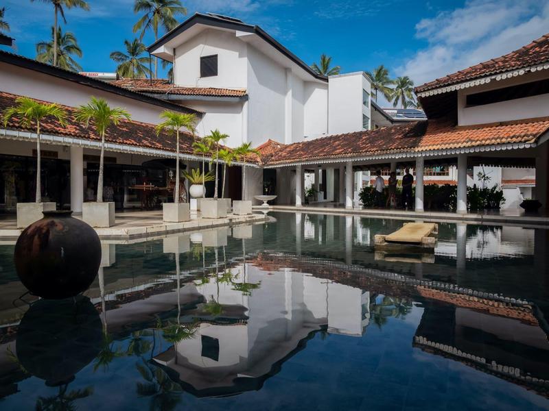 Luxusní hotel s bazénem, obklopený palmami a bíle omítnutými budovami pod modrou oblohou.