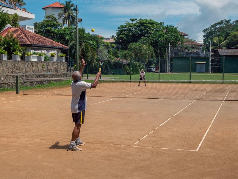 Dva lidé hrají tenis na antukovém kurtu pod modrou oblohou.