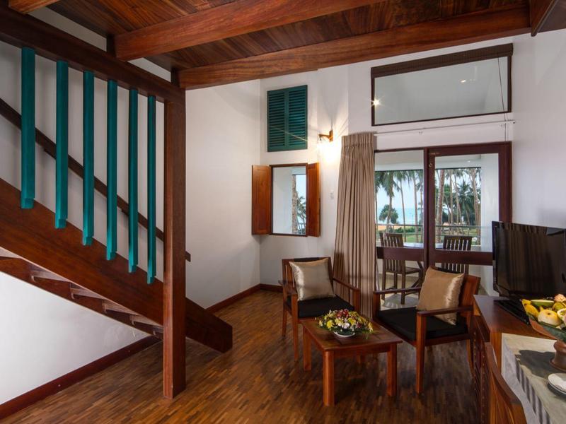 Pohodlný obývací prostor s dřevěným nábytkem, jídelním stolem a schodištěm se zeleným zábradlím.