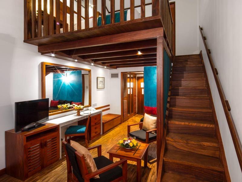 Obývací pokoj s dřevěným schodištěm do galerie, dřevěným nábytkem a světlými stěnami.