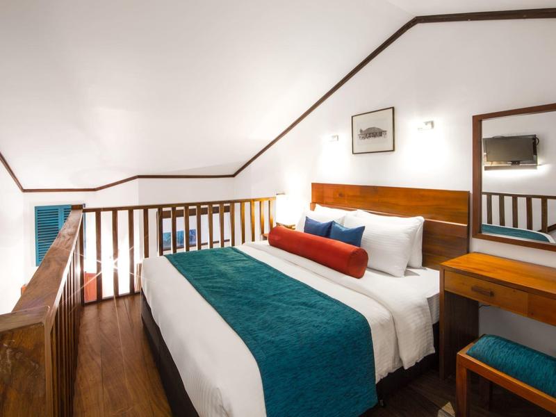 Přátelský hotelový pokoj s manželskou postelí a dřevěnou výzdobou pod šikmým stropem.