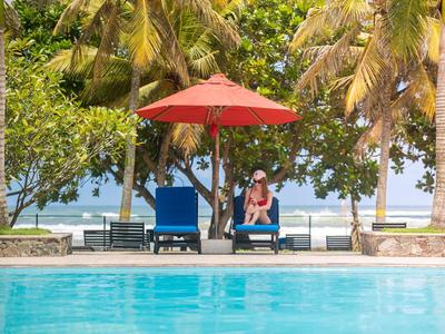 Pool mit blauem Wasser, zwei blauen Liegestühlen, rotem Sonnenschirm und Palmen am Strand.