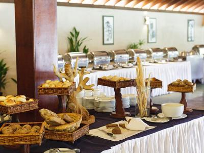 Buffet mit Brötchen, Brotstangen und warmen Speisen in silbernen Behältern auf weißen Tüchern.